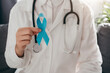 © Yura Yarema - Close up of professional female doctor in uniform and stethoscope holding light blue ribbon awareness. Men's health and Prostate cancer awareness campaign in November month. Symbol of medical issues