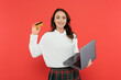 Smiling woman in jumper holding credit card and laptop isolated on red