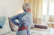 © Jelena Stanojkovic - Woman feels back pain, massaging aching muscles. Mature woman feeling morning discomfort in aching back in the living room.