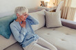 © Jelena Stanojkovic - Photo of senior woman suffering from chest pain while sitting on sofa at home during the day. Old age, health problem and people concept - close up of senior woman suffering from heartache at home.