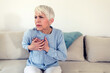 © Jelena Stanojkovic - Shot of a beautiful matre woman holding her chest in discomfort due to pain at home during the day. A stressed woman who is suffering from a chest pain and touching her heart area.
