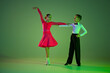 Studio shot of graceful little boy and girl dancing ballroom dance isolated over green background in neon light. Concept of art, beauty, grace, action, emotions.