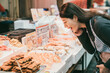 © PR Image Factory - closeup of amazed asian girl looking at delicious traditional processed seafood on display at a vender while shopping at kuromon ichiba market in Osaka japan