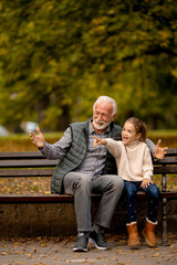 Wall Mural - Grandfather spending time with his granddaughter on bench in park on autumn day