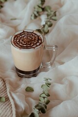 Canvas Print - Cup of coffee with chocolate spider web on white and brown textile covered with decorative leaves