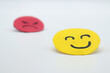 © PHalexaviles - Yellow cut out paper smiley face with another red angry face in the background. on white background. concept of envy, selfishness, happiness or well-being