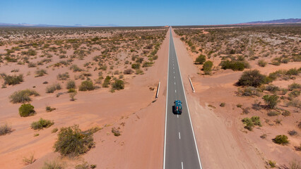 Poster - Aerial view of a green campervan on a long straight through a desert of red sand