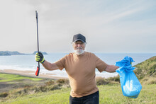Positive Senior Man Standing On Hill With Trash Tongs And Sack