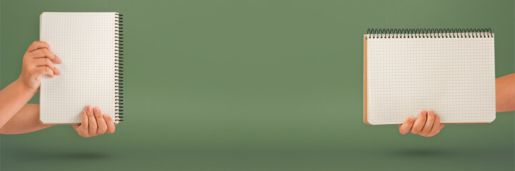 Wall Mural - Notepad in hand. Blank notepad in the hands on a green background. Hands hold a book without text. The girl is holding a book with an empty cover.