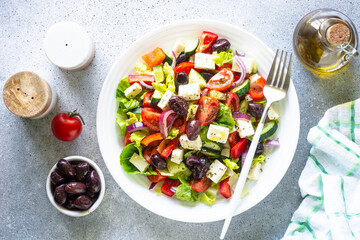 Poster - Greek salad with olives, feta cheese and fresh vegetables. Top view on light stone table.