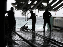 Silhouettes Of Persons Recovering Source (gun) Array On Seismic Survey Vessel. Sources Are Used To Produce Underwater Acoustic Sound Waves With High Pressure Air.