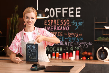 Sticker - Young female barista pointing at chalkboard with menu in cafe