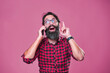 Bearded man with glasses coming up with solution, idea realization while talking on the phone; pink studio background
