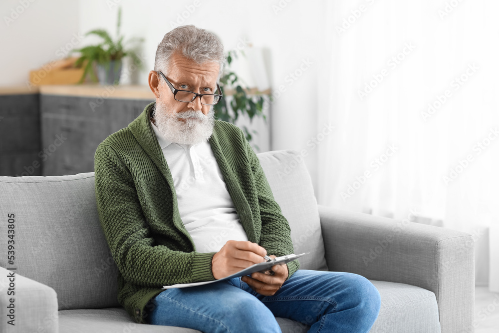 Male psychologist with clipboard video chatting in kitchen