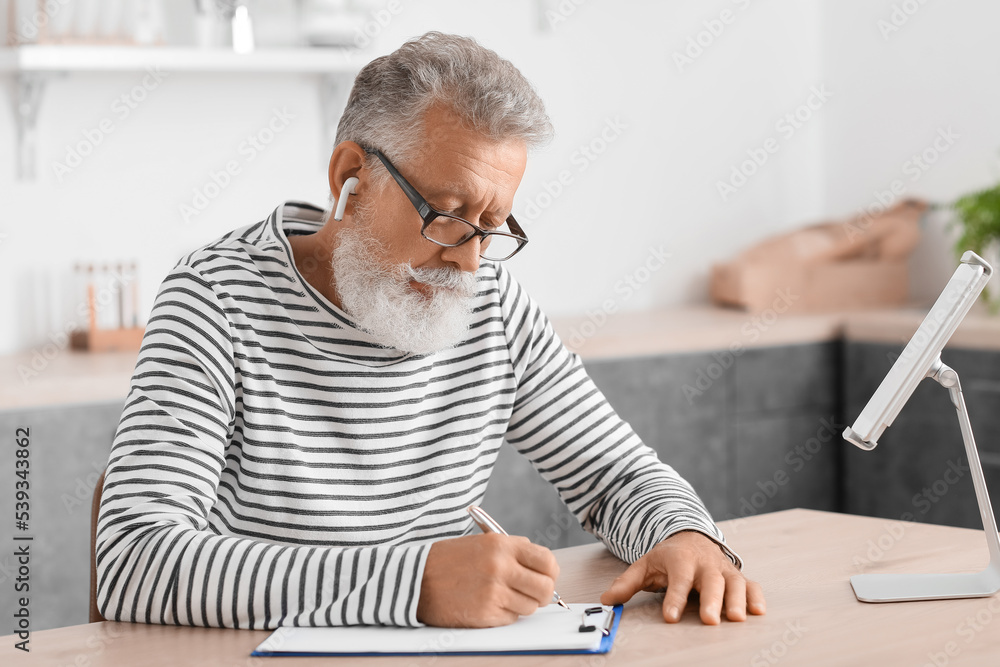 Male psychologist with tablet computer video chatting at table in kitchen
