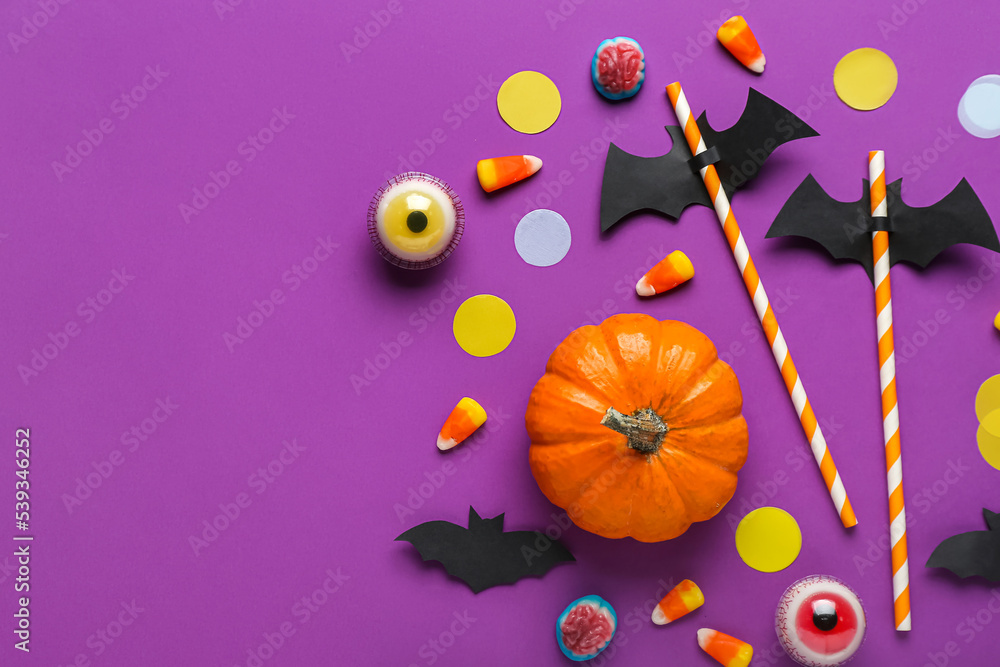 Paper bats with straws, candy corns and Halloween decor on purple background
