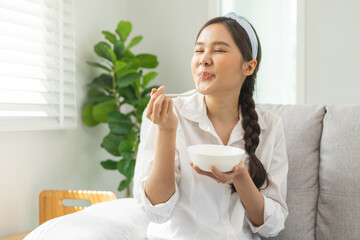 Wall Mural - Healthy lifestyle, wellness food asian young woman hand use spoon eat tasty fresh organic yogurt, dairy product in bowl breakfast meal at home. Snack tasty on diet nutrition delicious natural yoghurt