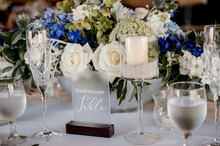 Sweetheart Sign On Table With Blue And White Wedding Floral Centerpiece On White Table Cloth Surrounded By Place Settings And Glassware. Blue Hydrangeas White Roses Horizontal No People