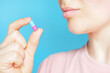 © TATIANA - Young woman holding a capsule on a blue background close-up.
