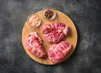 Wall Mural - Raw pork cheeks meat on a dark gray surface with spices. Top view. Food background
