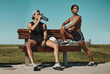 © Allistair F/peopleimages.com - Sports, bench and fitness people with water bottle in a park for outdoor training, workout or wellness with blue sky mock up. Athlete or runner couple relax together after running with summer mockup