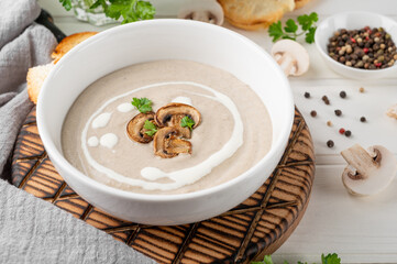 Wall Mural - Mushroom cream soup with cream, croutons and herbs on a white wooden background. Delicious comfort food.