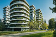 Modern residential buildings in the public green area. Apartment houses in Europe. Beautiful view of real estate homes in Milan, Italy. Business district in summer. Walking area with trees and grass.