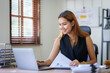 © amnaj - Young  Asian businesswoman who is happy to work in the office with a lot of paperwork arranged on the desk.