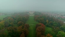 Mysterious Baroque Castle Slavkov Near Brno In The Fog. A Large Castle Garden With Autumn Colors And Dry Leaves. City In The Background.