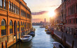Murano island, Venice, Veneto, Italy. View at bell tower brick building from the channel street with motorboats. Wooden dock with boats on the water and scenic sky with summer clouds sunset.