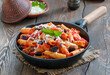 Pasta Alla Norma. Delicious sicilian pasta dish with roasted eggplant, marinara tomato sauce, grated ricotta and fresh basil served in frying pan with bowl of grated cheese.