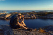 © Francis - A caucasian man with a straw hat sitting on a rock by the sea with backpack at sunrise.