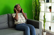 © fotofabrika - African woman listening to music with headphones while sitting on couch at home