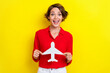 © deagreez - Portrait of satisfied positive gorgeous girl with bob hairdo dressed red shirt hold white paper plane isolated on yellow color background