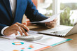 © Thapana_Studio - Businessman analyzing financial balance sheet and corporate profit report graph at office, calculating long term investment financial data, economic concept. stock market research and banking.