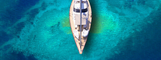 Canvas Print - Aerial drone ultra wide top down photo with copy space of beautiful luxury sail boat with wooden deck anchored in turquoise paradise island beach forming a blue lagoon