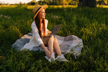 Wall Mural - portrait of smiling female tourist in straw hat and white dress sitting on field with green grass wi