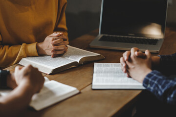 Christian group of people holding hands praying worship together to believe and Bible on a wooden table for devotional for prayer meeting concept.