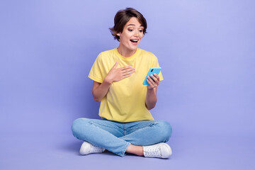 Poster - Full length portrait of impressed cheerful person sit floor use telephone isolated on purple color background