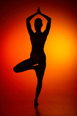 Wall Mural - Silhouette of female full-length body isolated over orange background. Standing on yoga pose