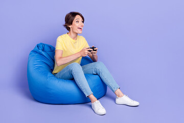 Canvas Print - Full body portrait of overjoyed positive lady sitting comfy bag play games isolated on purple color background