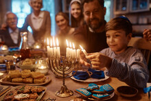 Jewish Son And Father Lighting Menorah During Family Meal On Hanukkah.