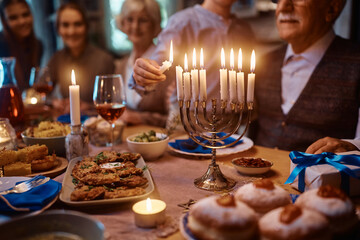 Wall Mural - Close up of kid lighting the menorah during family dinner on Hanukkah.