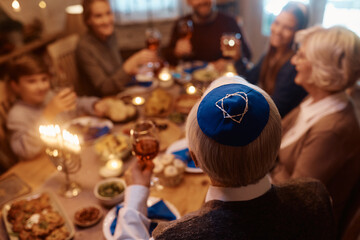 Wall Mural - Rear view of senior Jewish man toasting with his family during meal at dining table on Hanukkah.