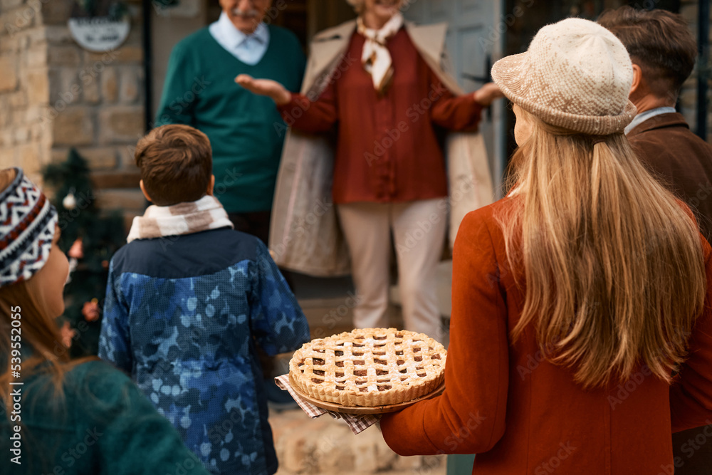 Rear view of woman carrying pie while visiting grandparents with her family for Thanksgiving.