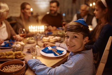 Wall Mural - Happy Jewish boy having family dinner at dining table on Hanukkah and looking at camera.