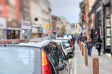 A Typical Busy High Street Scene In The UK With Parked Cars And Pedestrians.