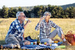© pucko_ns - Senior couple in nature enviroment drink vine and make picnic on blanket with food, relaxed and fun