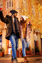 Couple having fun drinking mulled wine and walking down decorated city streets for Christmas