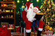 © ZaStock - Santa Clause reads a book to a little boy while sitting near Christmas tree. New Year concept